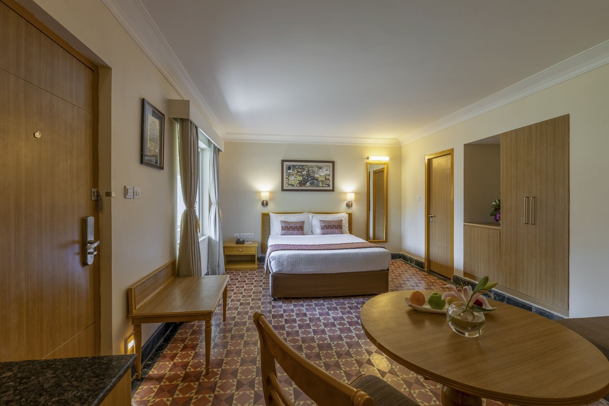 A hotel room with a bed, a dining table, a chair, a small table, and a cabinet.