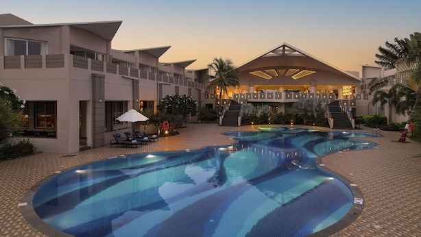 Un hôtel doté d’une grande piscine extérieure, de plusieurs niveaux de balcons et de palmiers.
