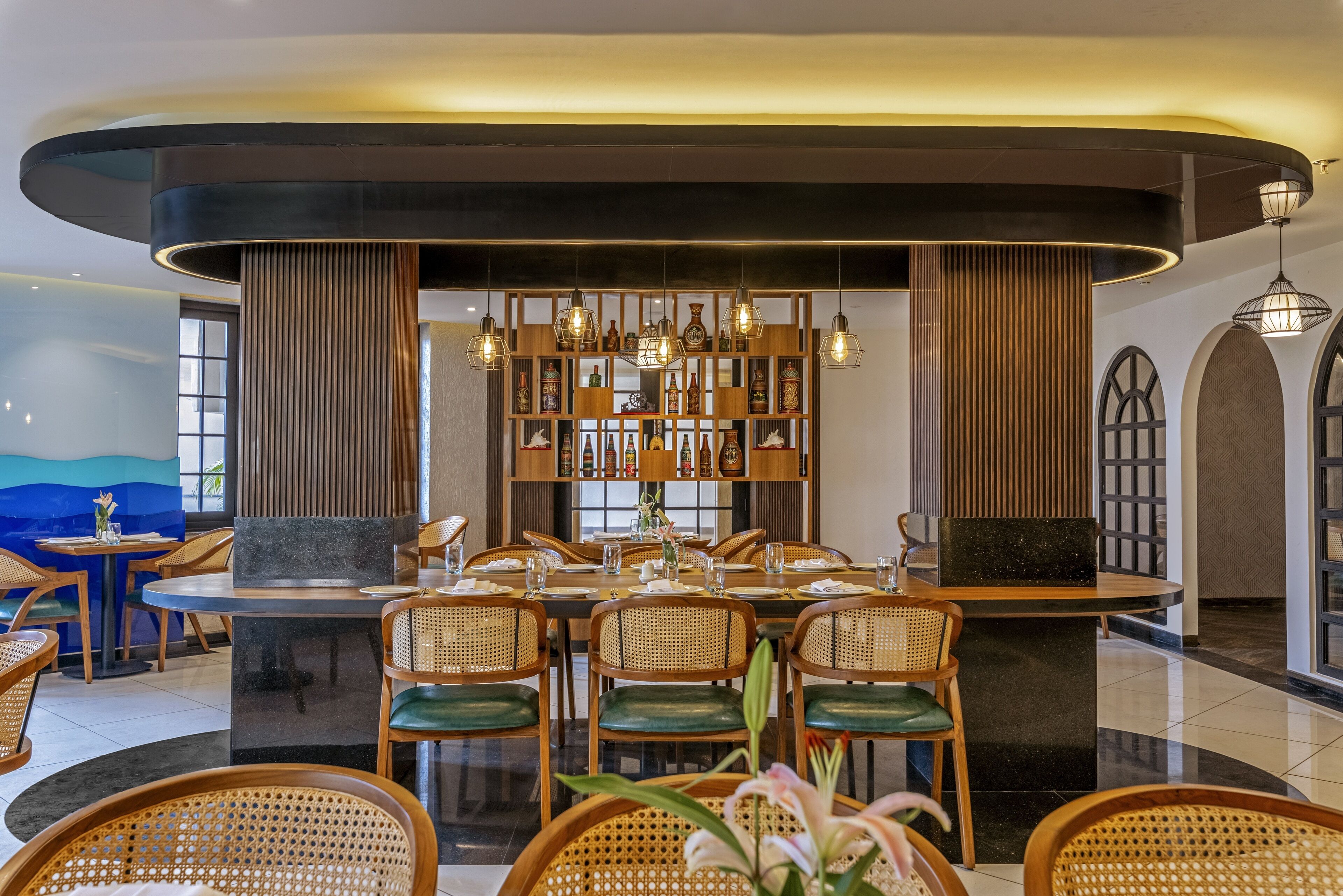 Een moderne eetruimte met ronde tafels, rieten stoelen en een centraal decoratieve presentatie.