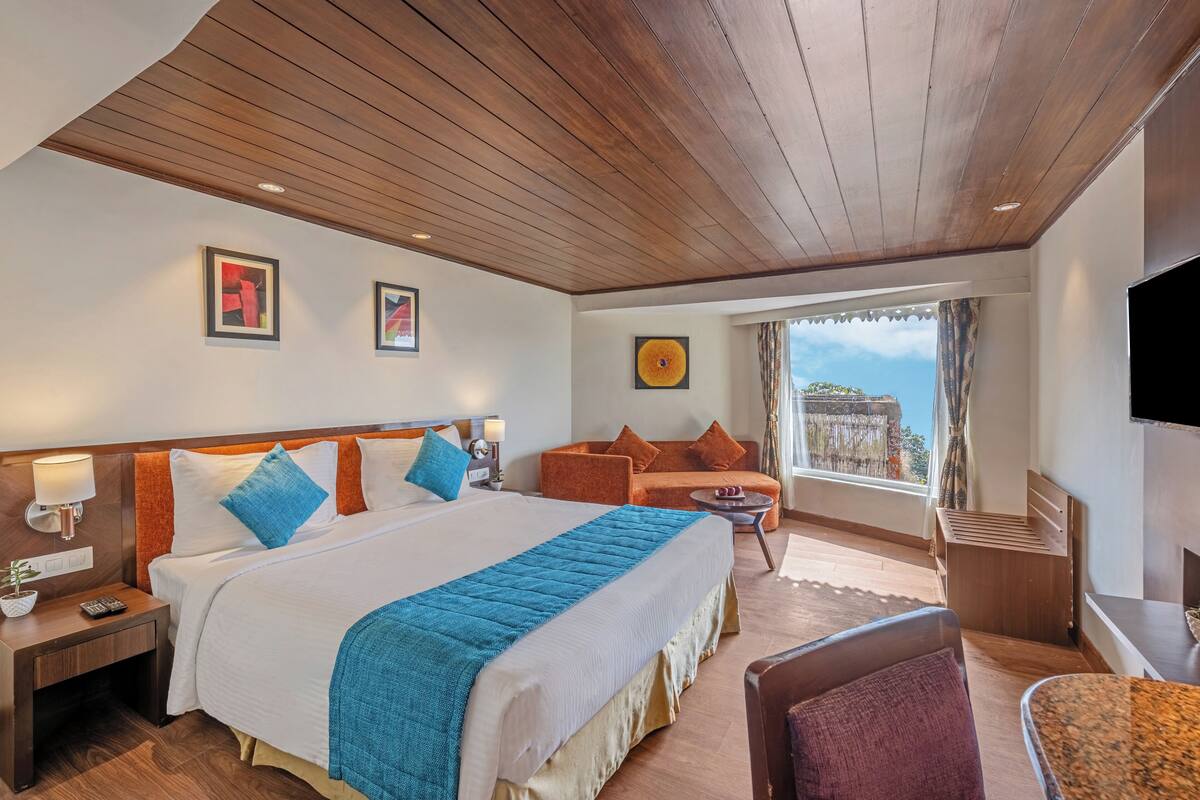 A hotel room with a large bed, a sofa, a TV, and a balcony with a view.
