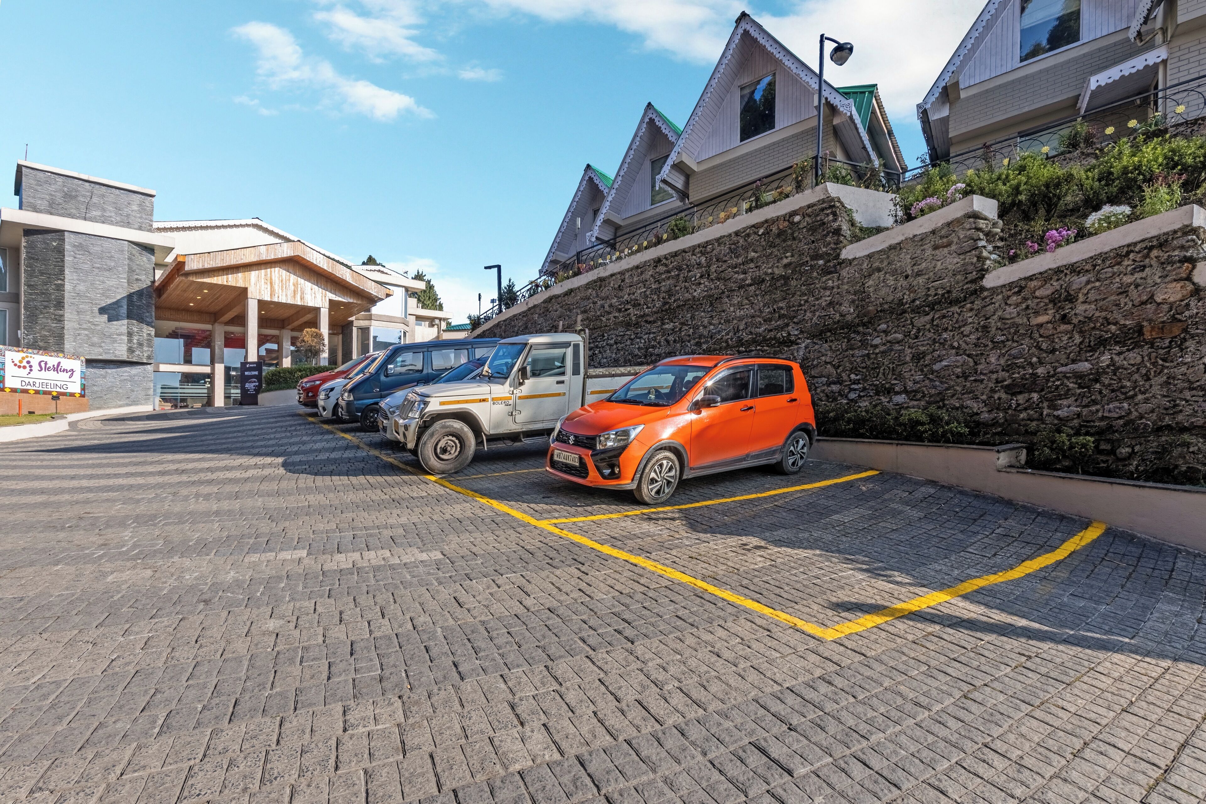A parking area with several cars, a building with a stone facade, and a sign for 'Stelling Darjeeling'.