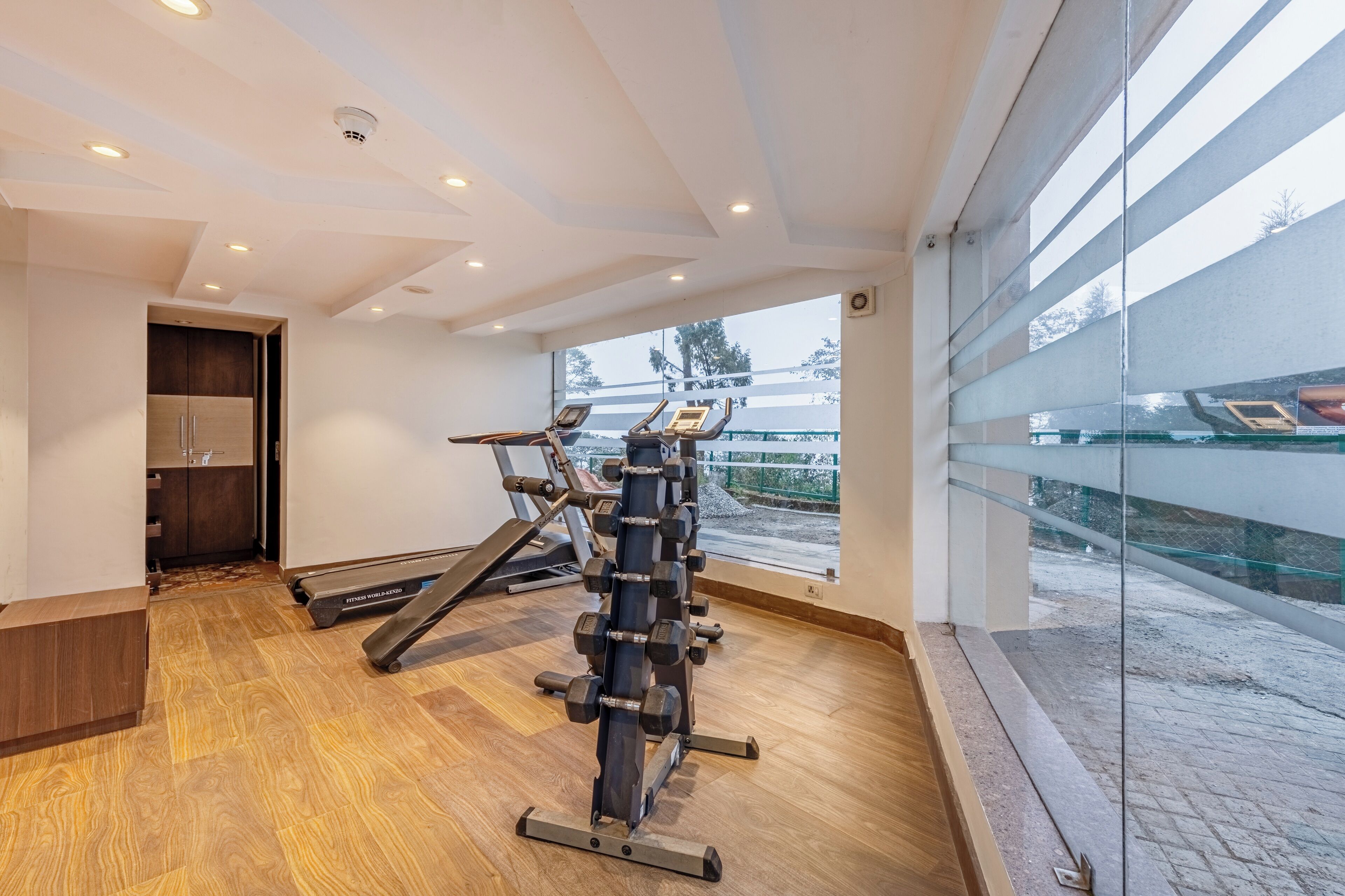 A gym with exercise equipment, a wooden floor, and a large window with a view of the outside.