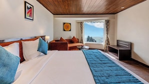 A hotel room with a large bed, a sofa, a small table, and a window with a view. - Sterling Darjeeling (Darjeeling)
