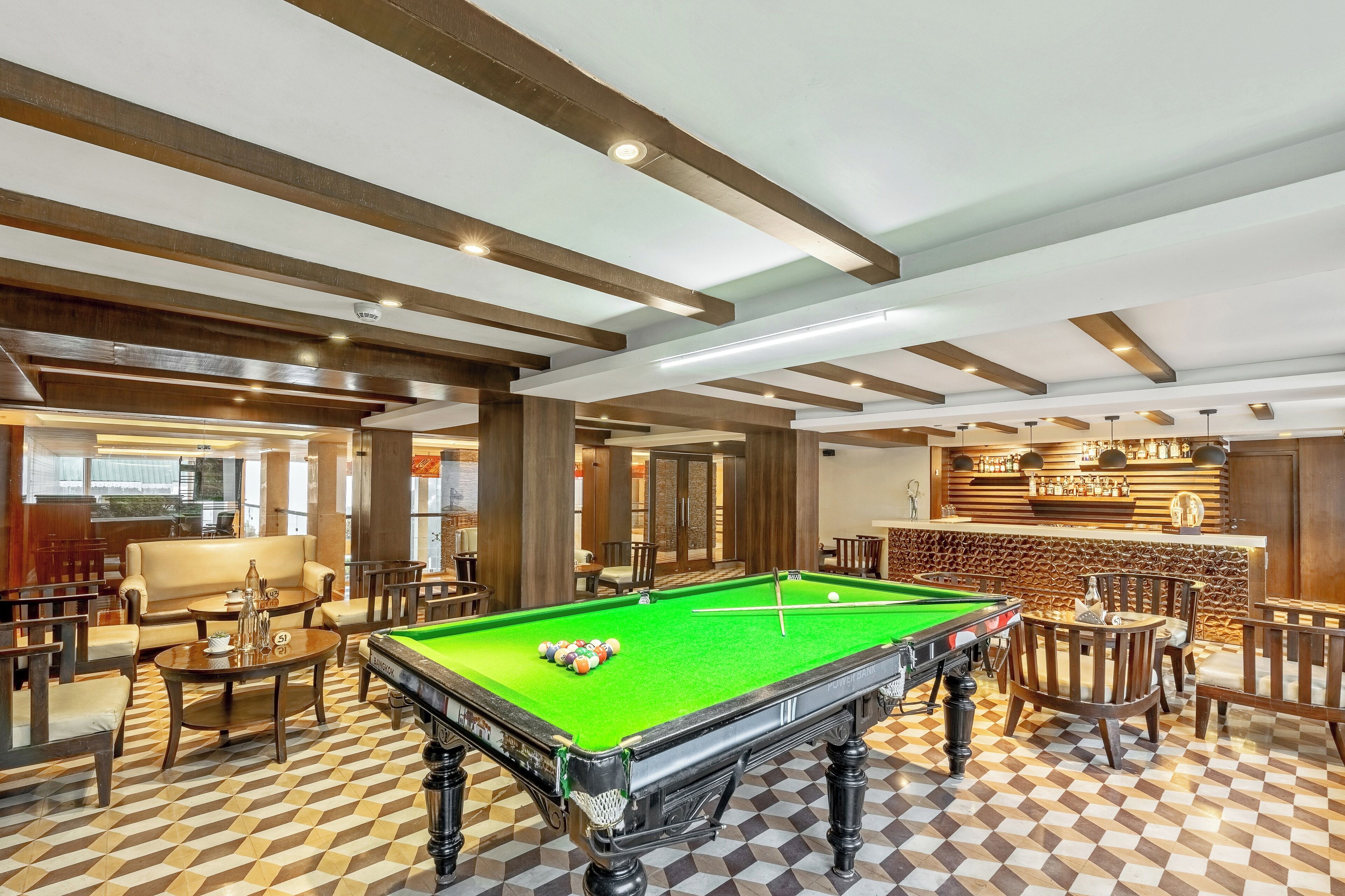 A pool table in a well-lit room with wooden beams on the ceiling, surrounded by chairs and tables.