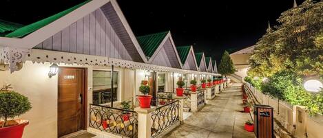 A row of hotel rooms with individual balconies, each with a potted plant and a small table.