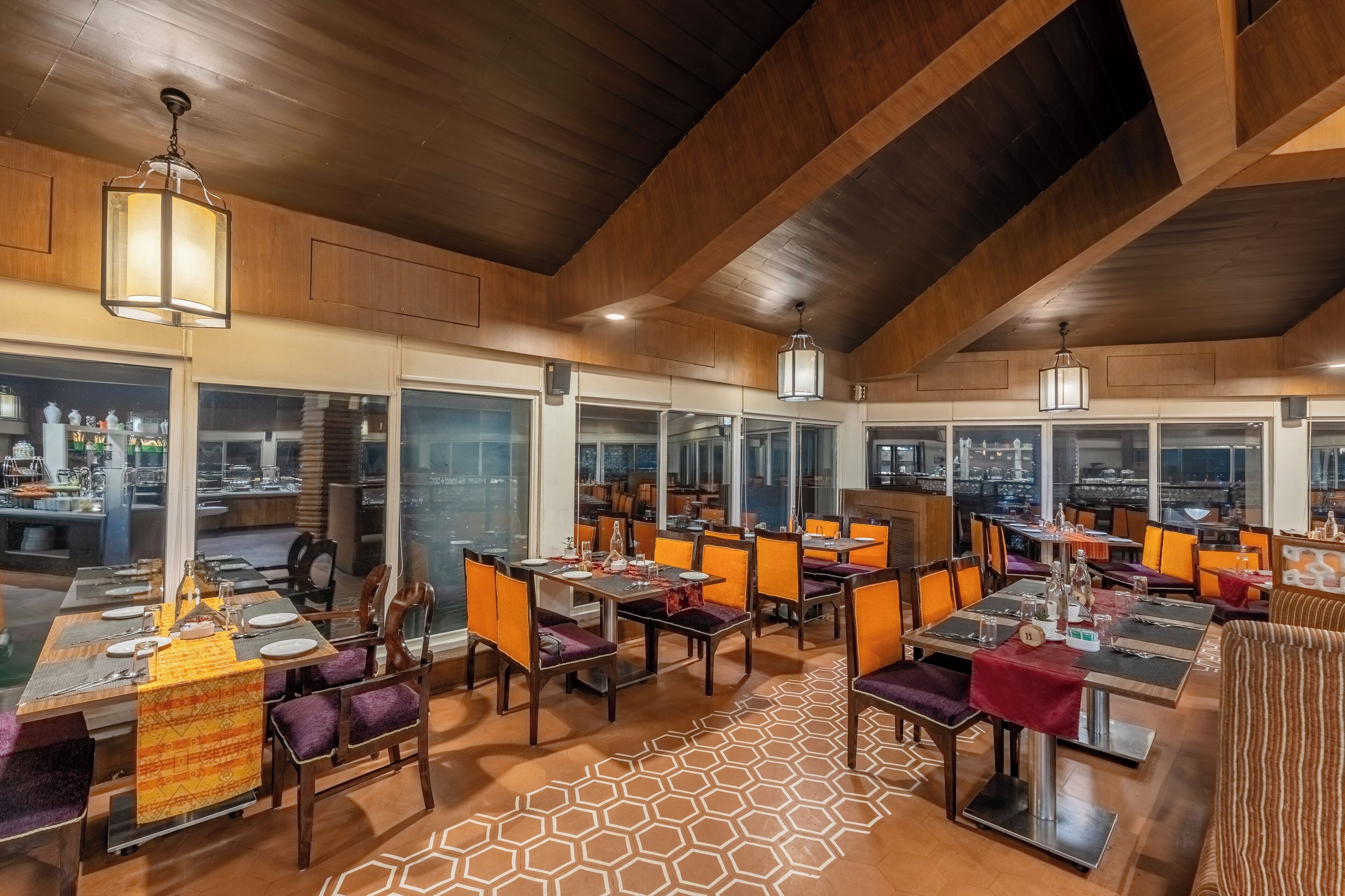 A modern restaurant with high ceilings and large windows. Tables are set with chairs, and the floor has a geometric pattern.