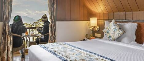A hotel room with a bed, a nightstand, a lamp, and a view of mountains through a window.