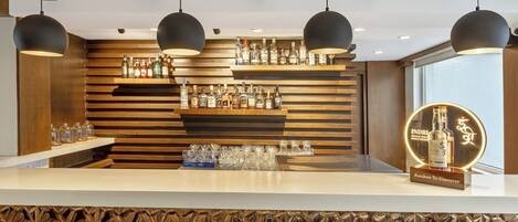 Zona de bar con listones de madera, lámparas colgantes y una exhibición de botellas de licor y vasos.