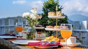 A table set with food and drinks, a tiered dessert stand, and a vase of flowers, with a scenic outdoor view in the background. - Sterling Darjeeling (Darjeeling)