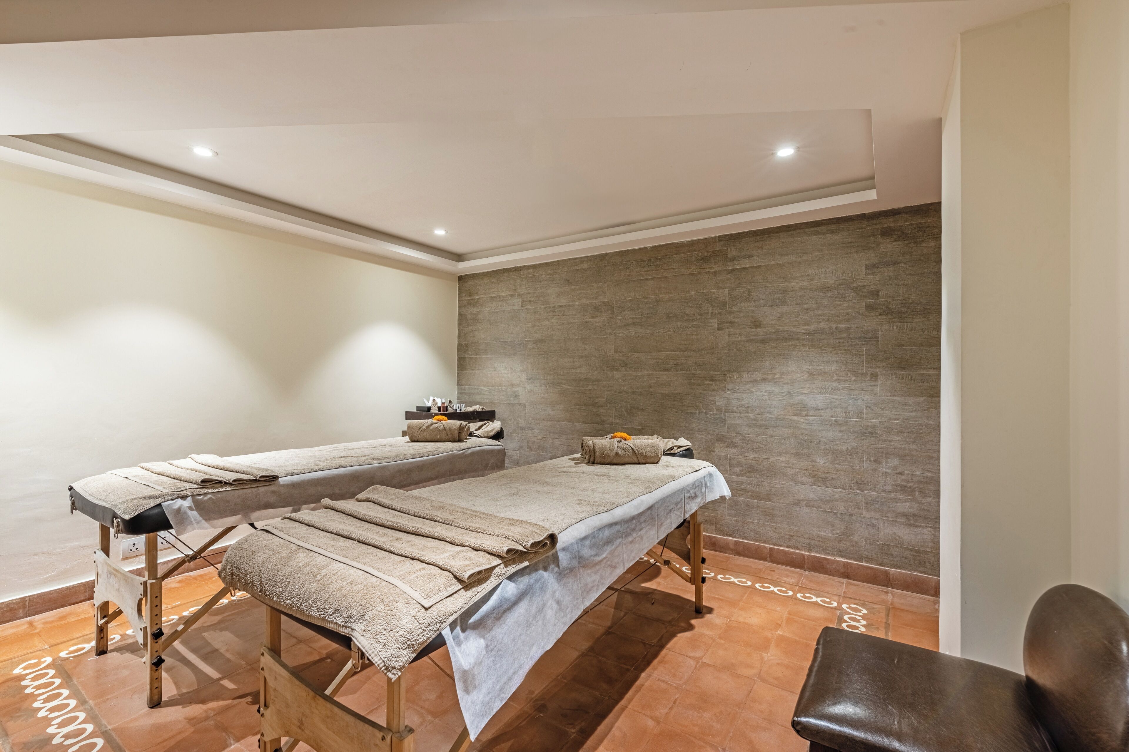 Ein Raum mit zwei Massagetischen, einem braunen Ledersessel und einer Steinwand.