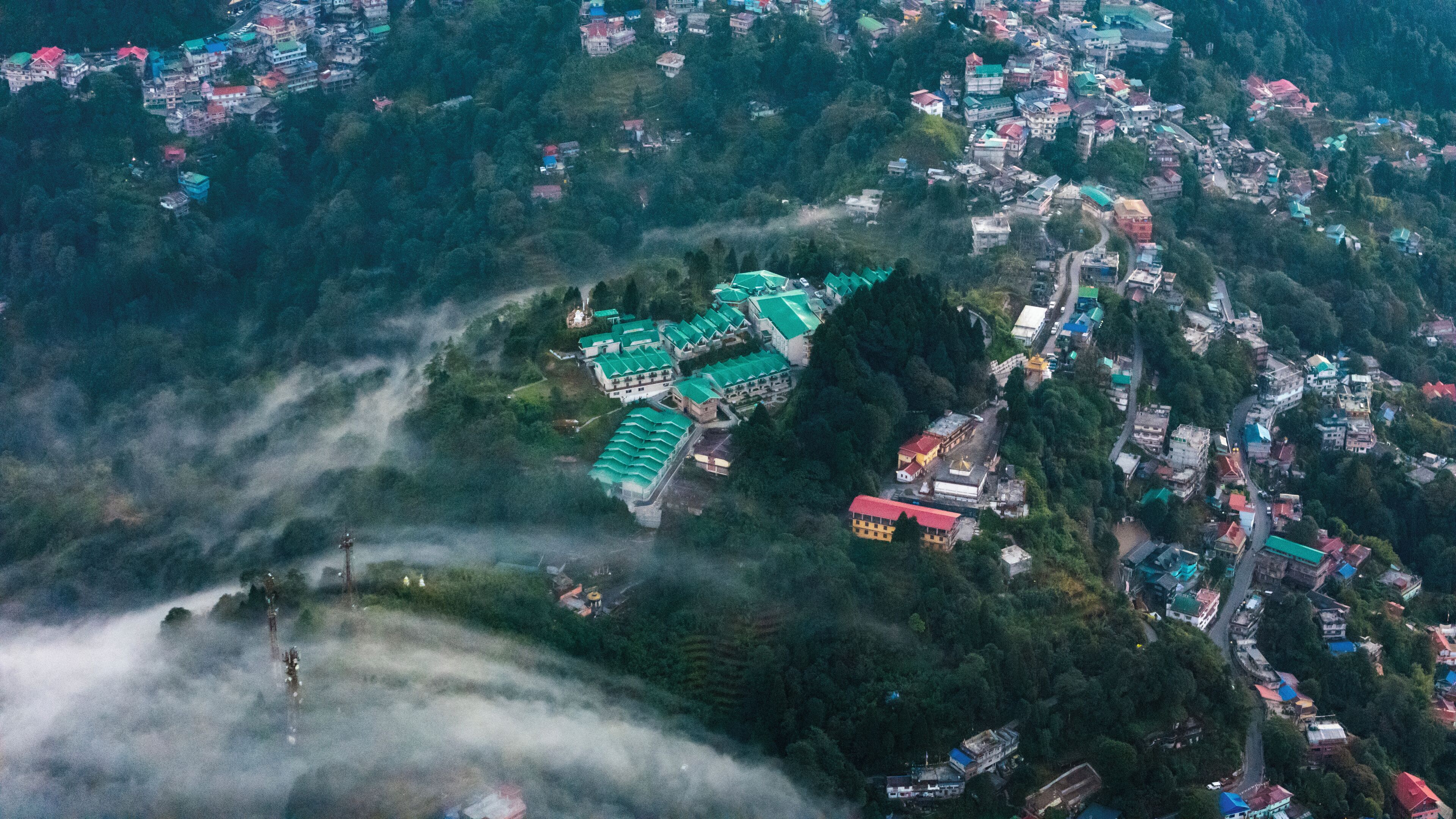 Vista aérea de un pueblo montañoso con casas tradicionales y un edificio destacado con techo verde.