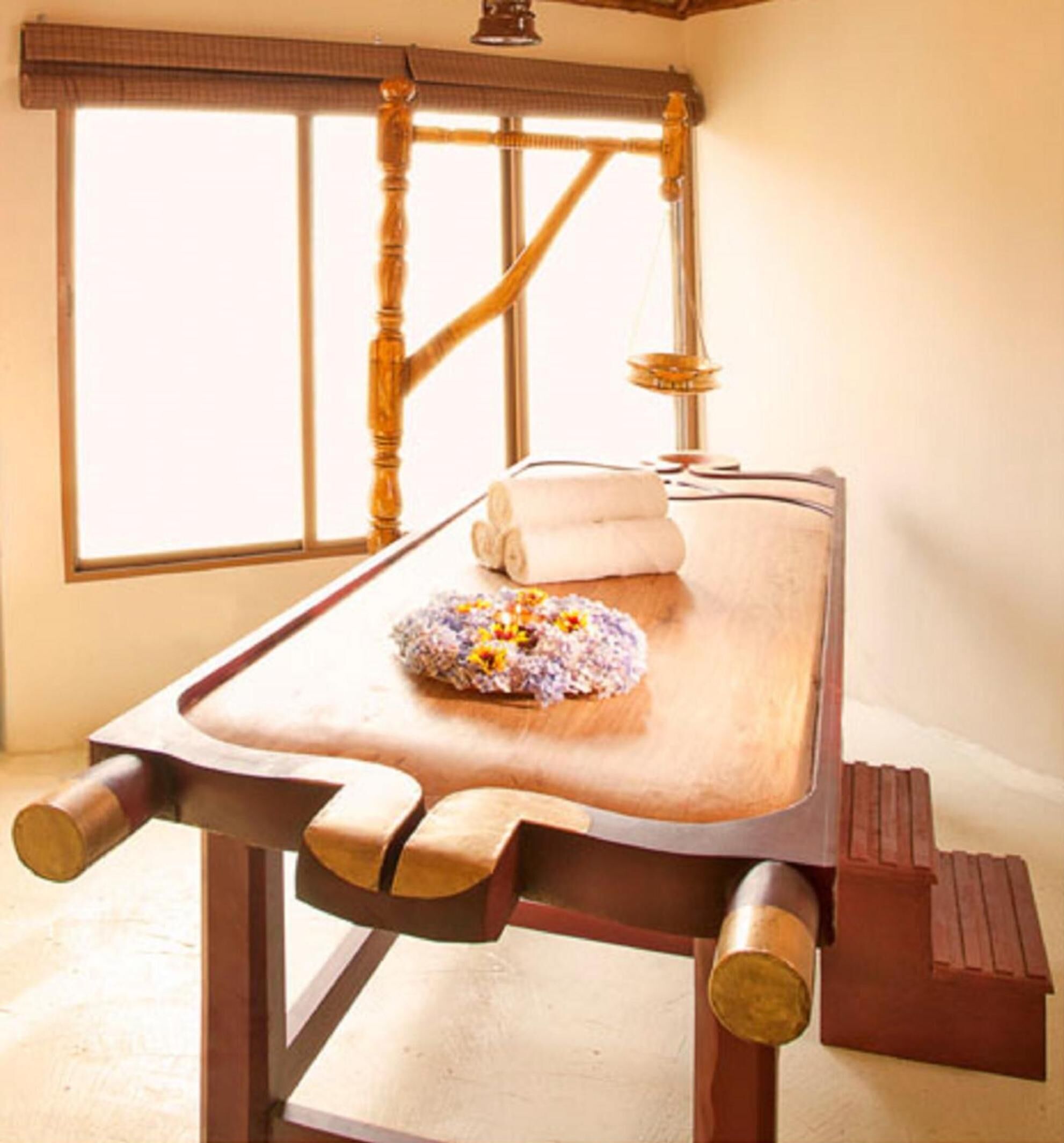 A wooden massage table with a towel and a flower arrangement.