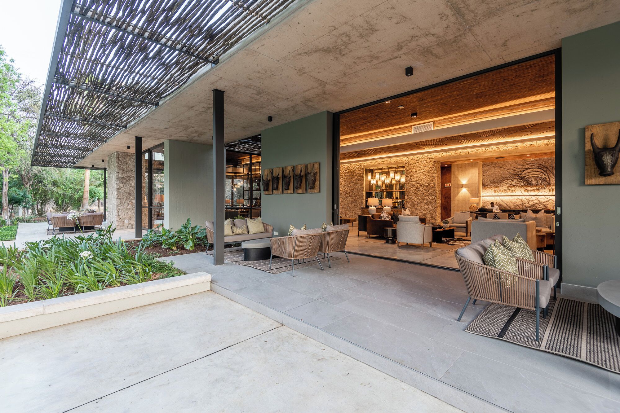 A modern outdoor living area with seating, a stone wall, and a well-lit interior space with furniture and decor.