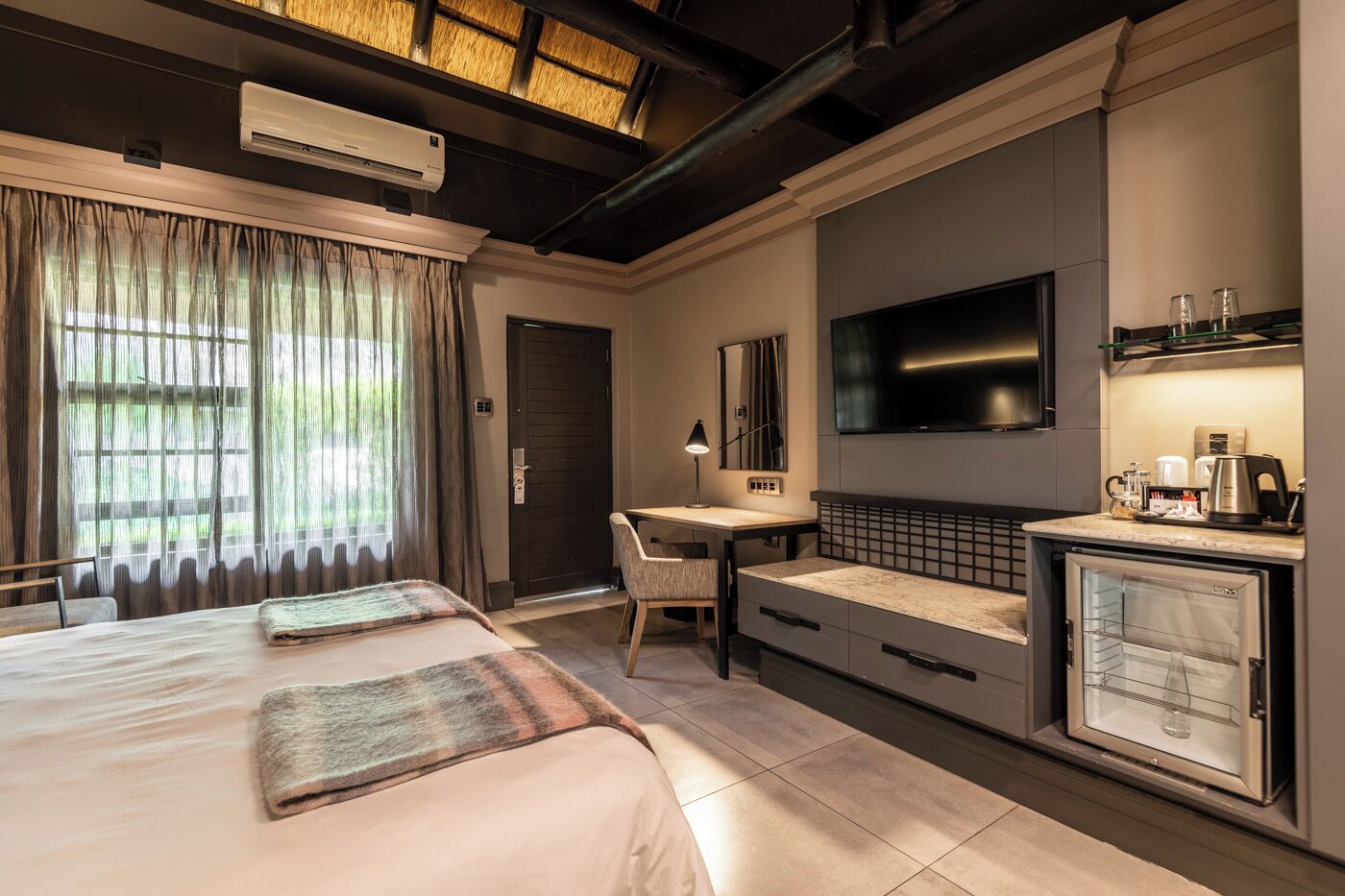 A hotel room with two beds, a desk, a TV, and a minibar.