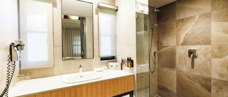 Un baño moderno con tocador de madera, un espejo grande, cabina de ducha de vidrio y zona de ducha con azulejos.