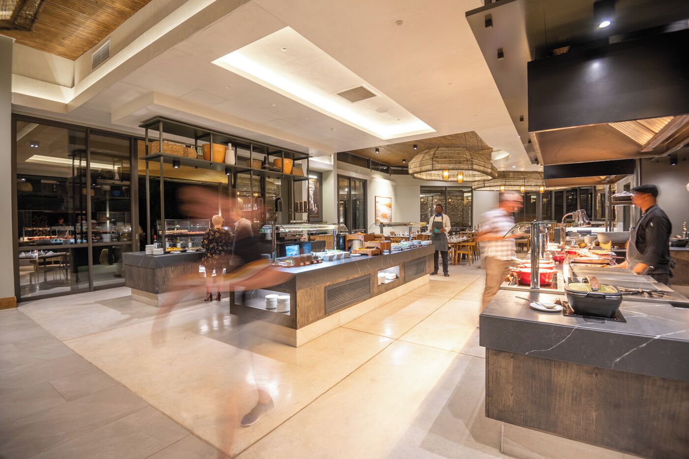 A modern restaurant with a central counter, glass display cases, and a high ceiling with recessed lighting.