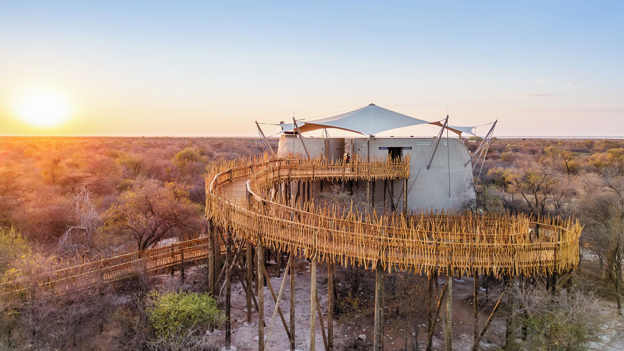 A circular wooden structure with a central building, surrounded by a natural landscape.