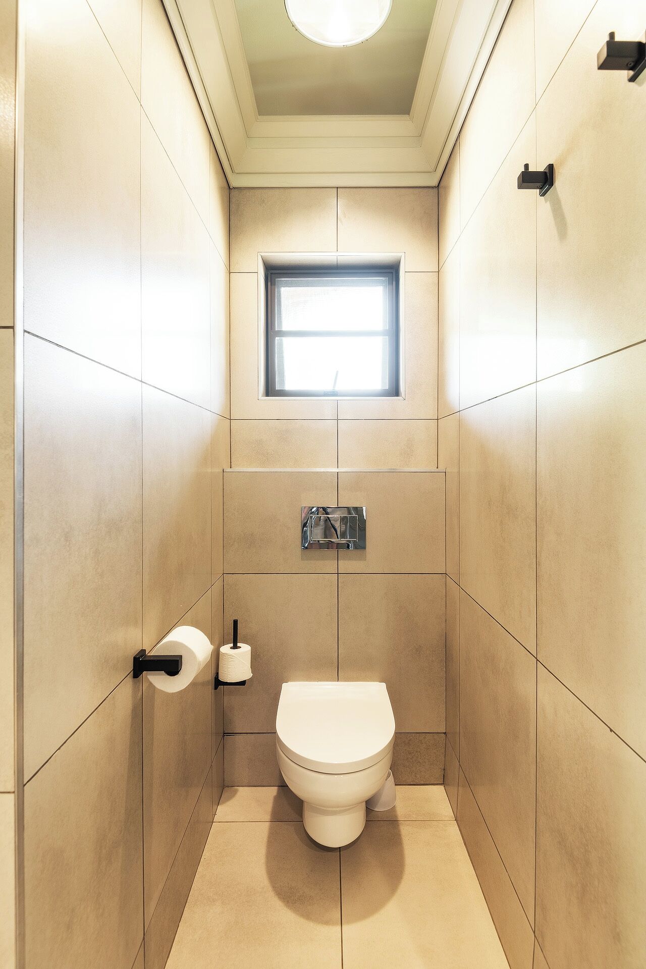 Un baño pequeño y moderno con inodoro, un dispensador de papel higiénico y una ventana.