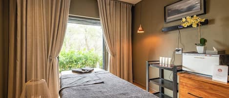 A bedroom with a bed, a bedside table with a lamp, a wall-mounted TV, and a window with curtains.