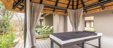 A spa room with a wooden deck, a massage table, and a thatched roof.