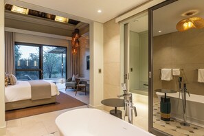 A modern hotel room with a large bed, a sitting area with a view, a separate bathroom with a bathtub, and a shower area. - Mokuti Etosha (Tsumeb)