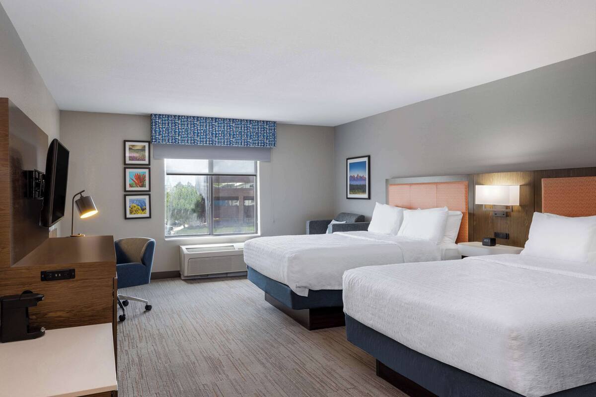 A hotel room with two beds, a desk, a chair, a TV, and a window with a view.