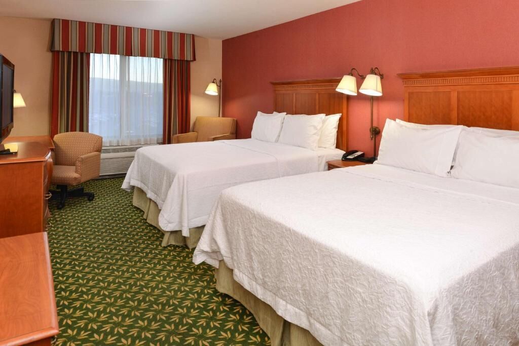 A hotel room with two beds, a desk, a chair, a TV, and a window with curtains.
