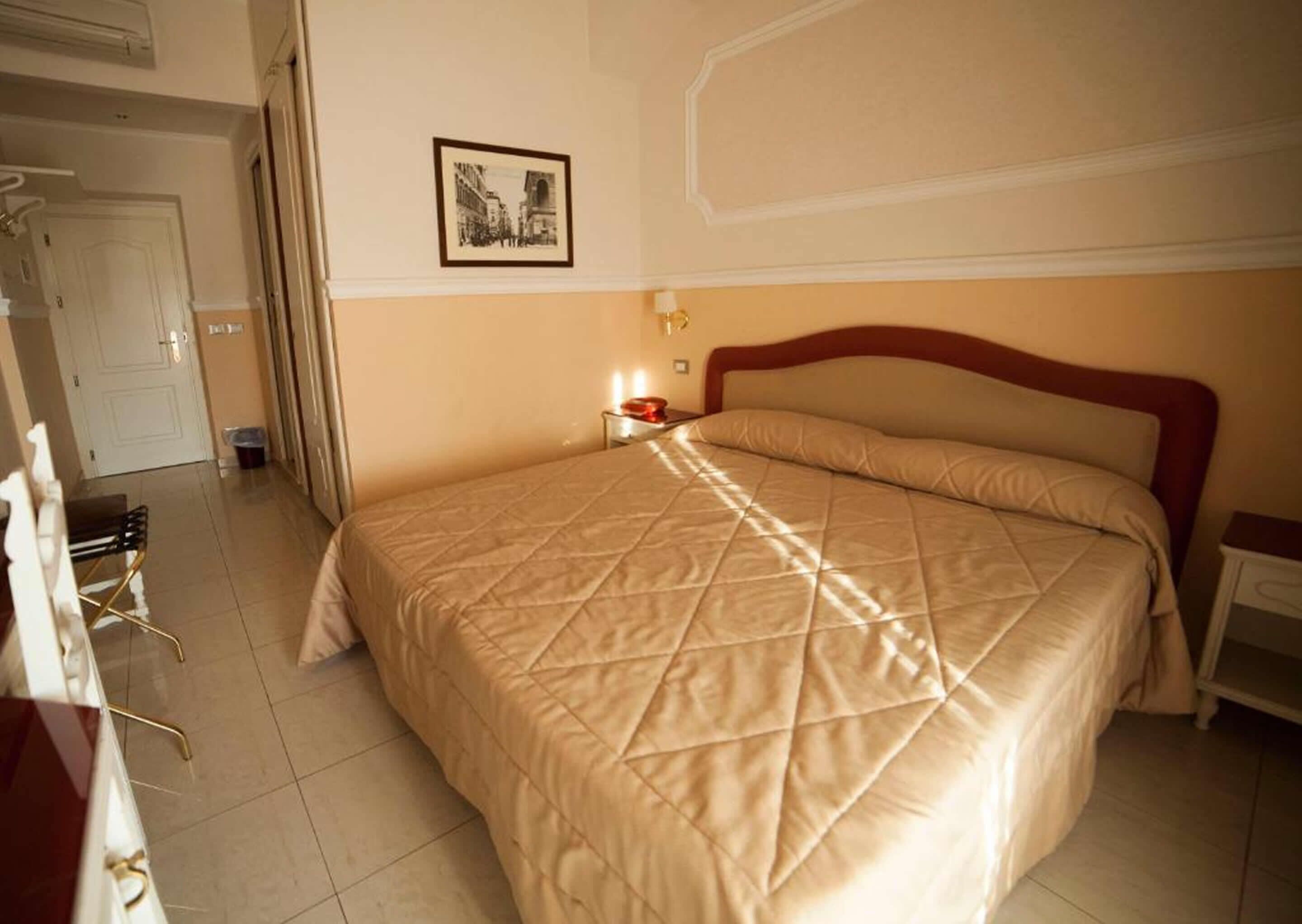 A hotel room with a large bed, a bedside table with a lamp, and a framed picture on the wall.
