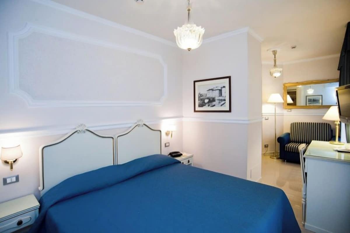 Une chambre d’hôtel comprenant un lit, une table de chevet, une lampe, une chaise et un miroir.