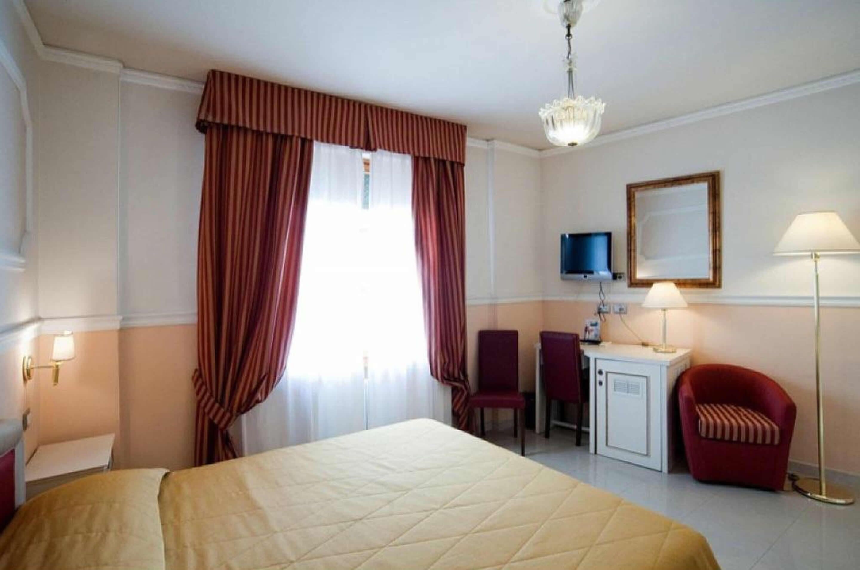 Una habitación de hotel con cama, escritorio, silla, televisor y lámpara.