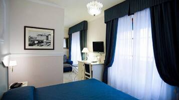 A hotel room with a bed, a desk, a chair, a television, and a chandelier.