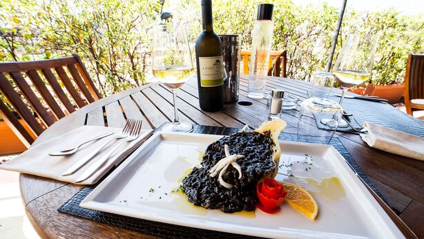 A dining table with a plate of food, wine glasses, and a bottle of wine.
