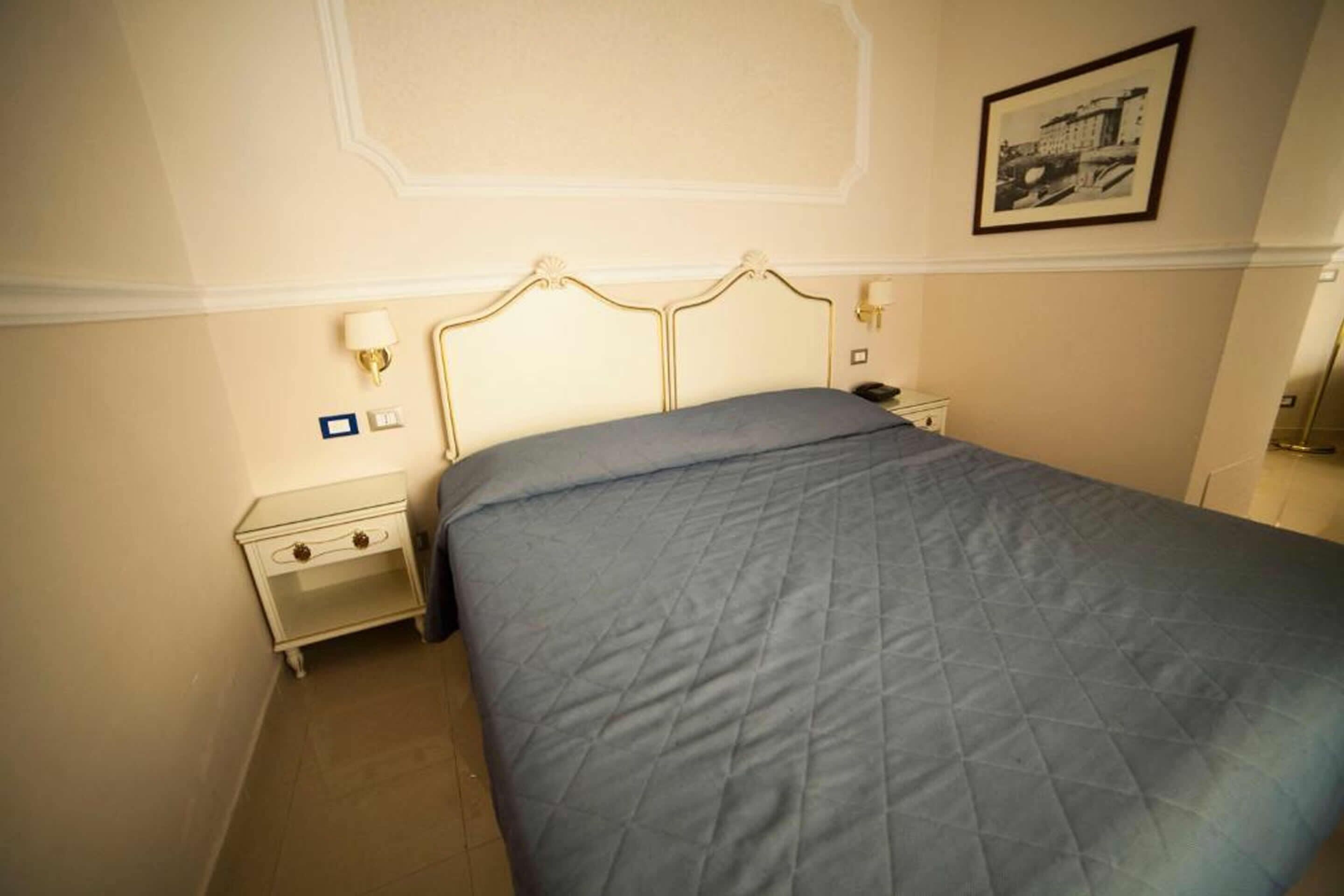 A bedroom with a bed, nightstands, a lamp, and a framed picture on the wall.