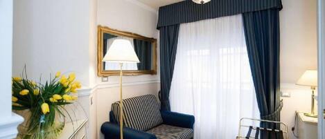 A room with a blue sofa, a standing lamp, a mirror, and a window with dark curtains.