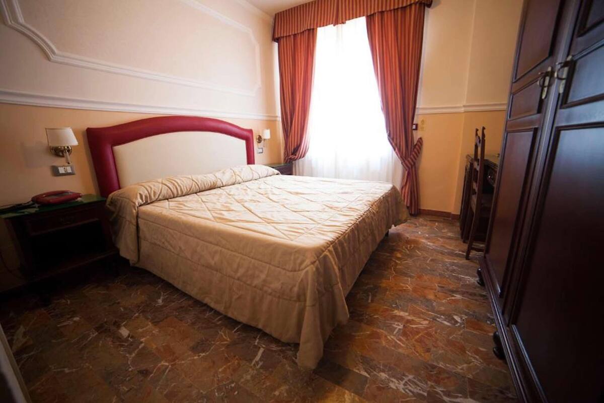 Une chambre d’hôtel avec un grand lit, une table de chevet, une lampe et une armoire.