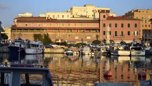 A marina with boats docked, a building with a sign reading "Ristorante," and a statue in the background.