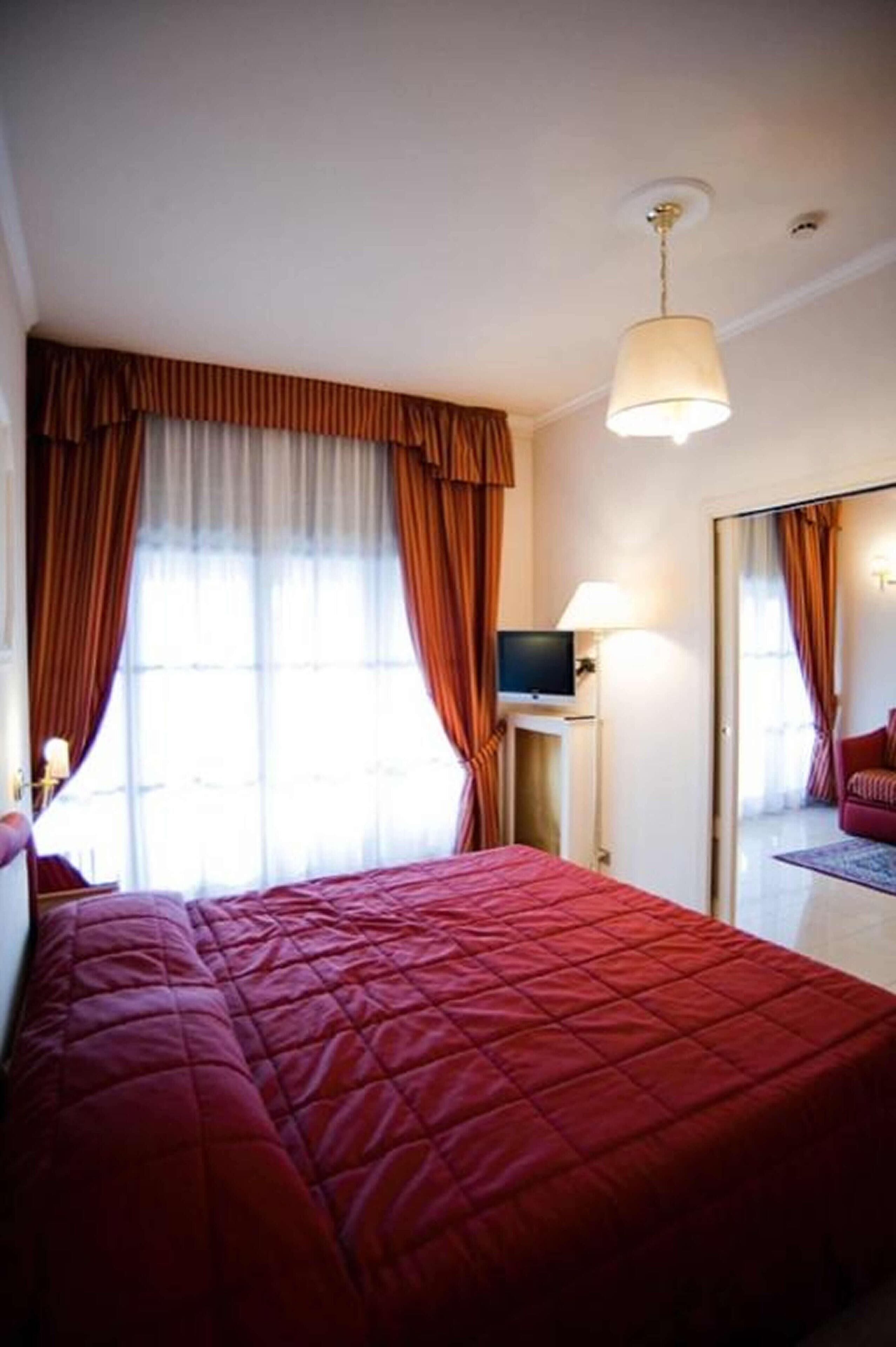 Una habitación de hotel con una cama grande, un televisor sobre una mesita y un espejo en la pared.