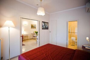 A hotel room with a bed, a desk, a chair, a lamp, and a bathroom visible through an open door.