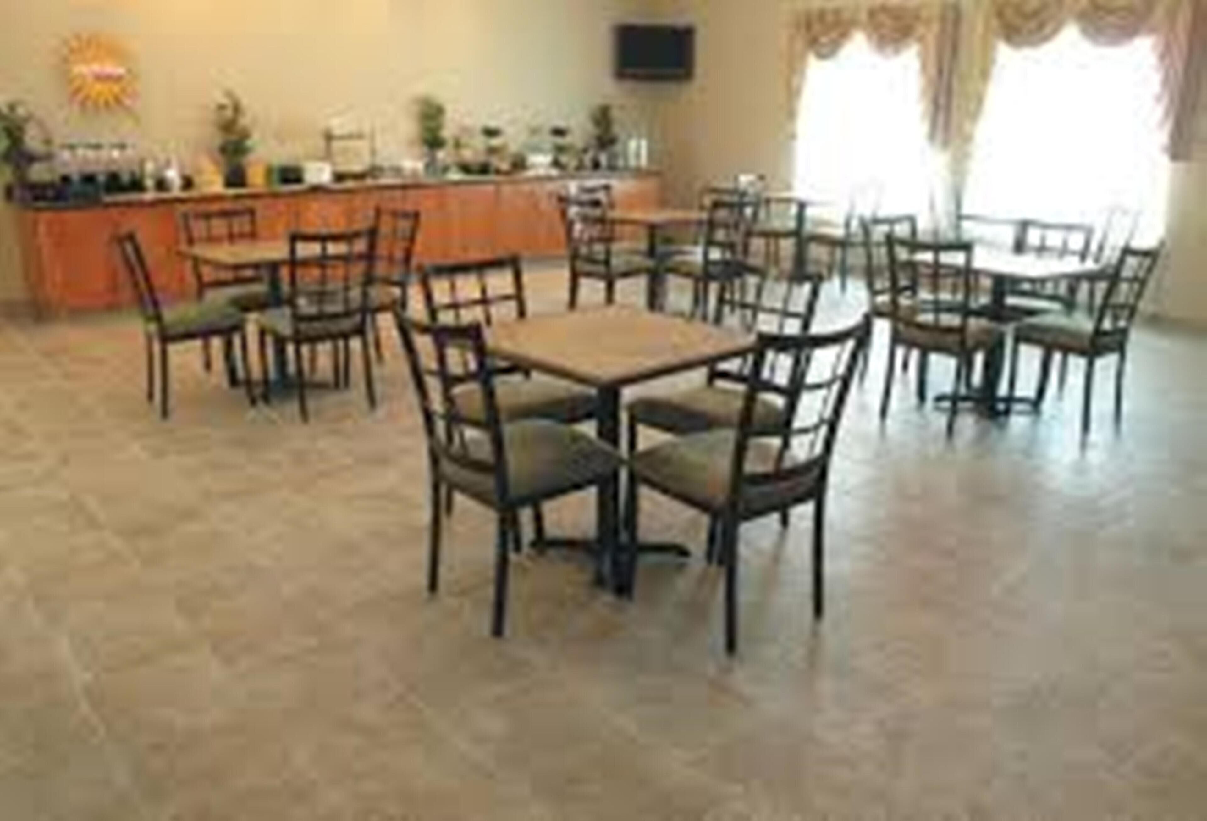 A dining area with multiple tables and chairs, a counter with a television, and a window with curtains.