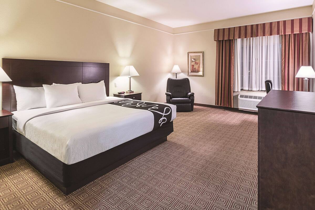 Habitación de hotel con una cama grande, una silla, un escritorio y una ventana con cortinas.