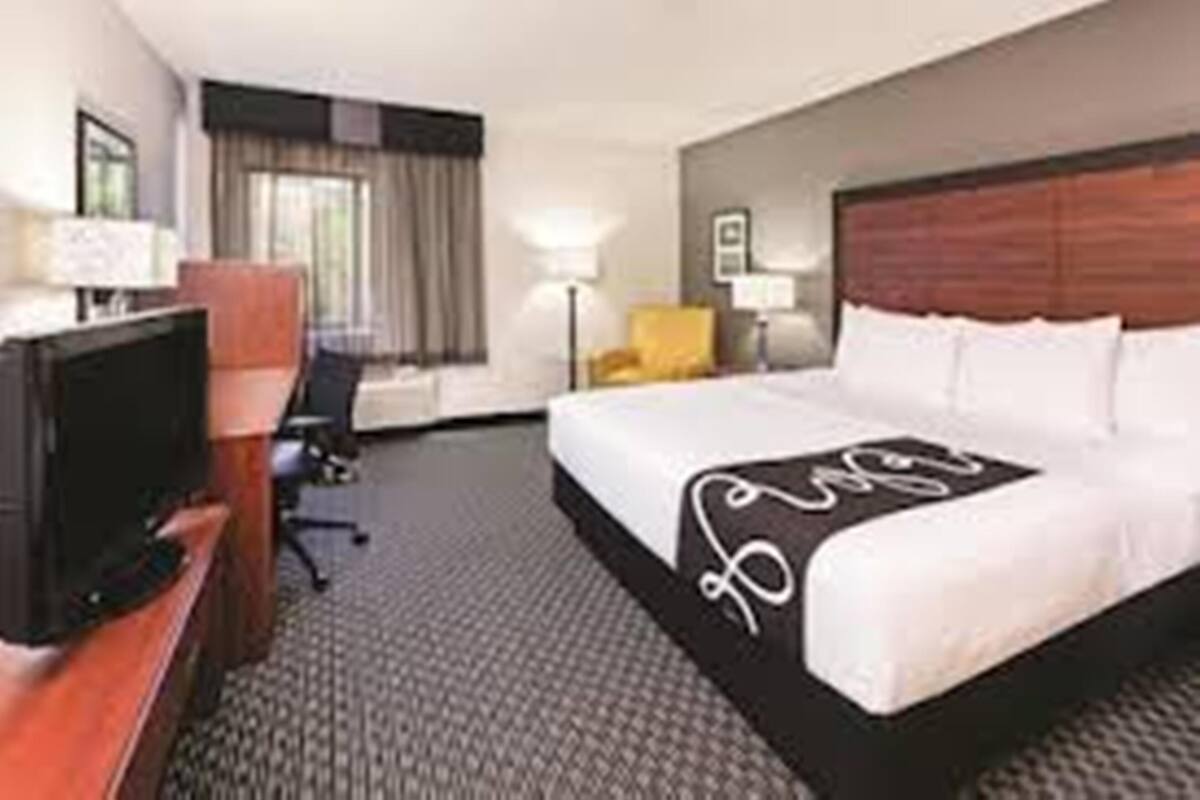 Una habitación de hotel con una cama, un escritorio con televisor, una silla y una lámpara.