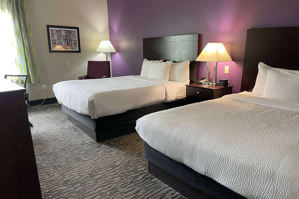 Habitación de hotel con dos camas, un escritorio y una silla. Hay dos mesitas de noche con lámparas.