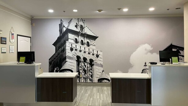 Zona d'entrada amb un mural gran d'un edifici, dues taules de recepció i un sostre amb il·luminació empotrada.