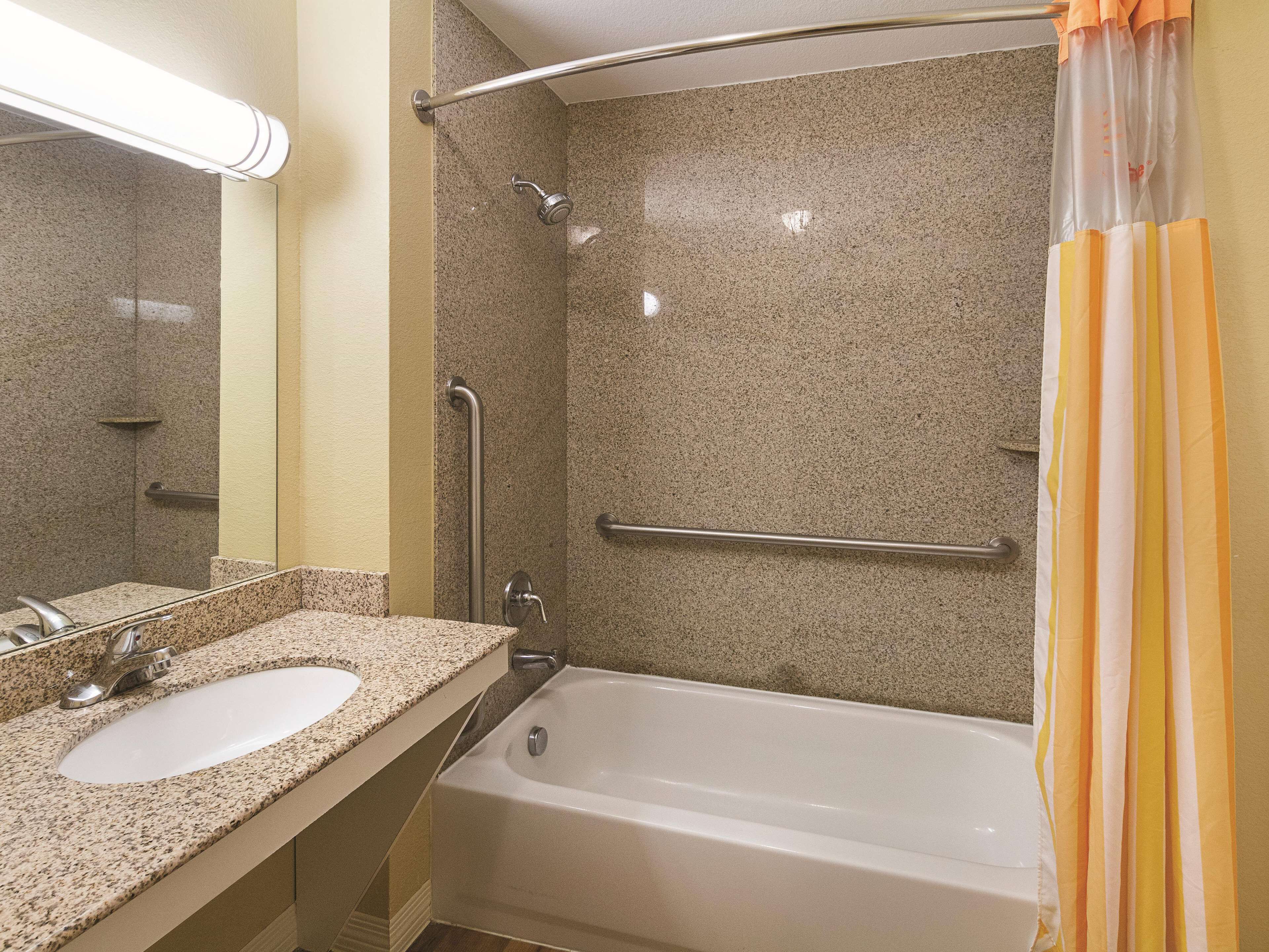 A bathroom with a granite countertop sink, a white bathtub, and a shower with a grab bar.