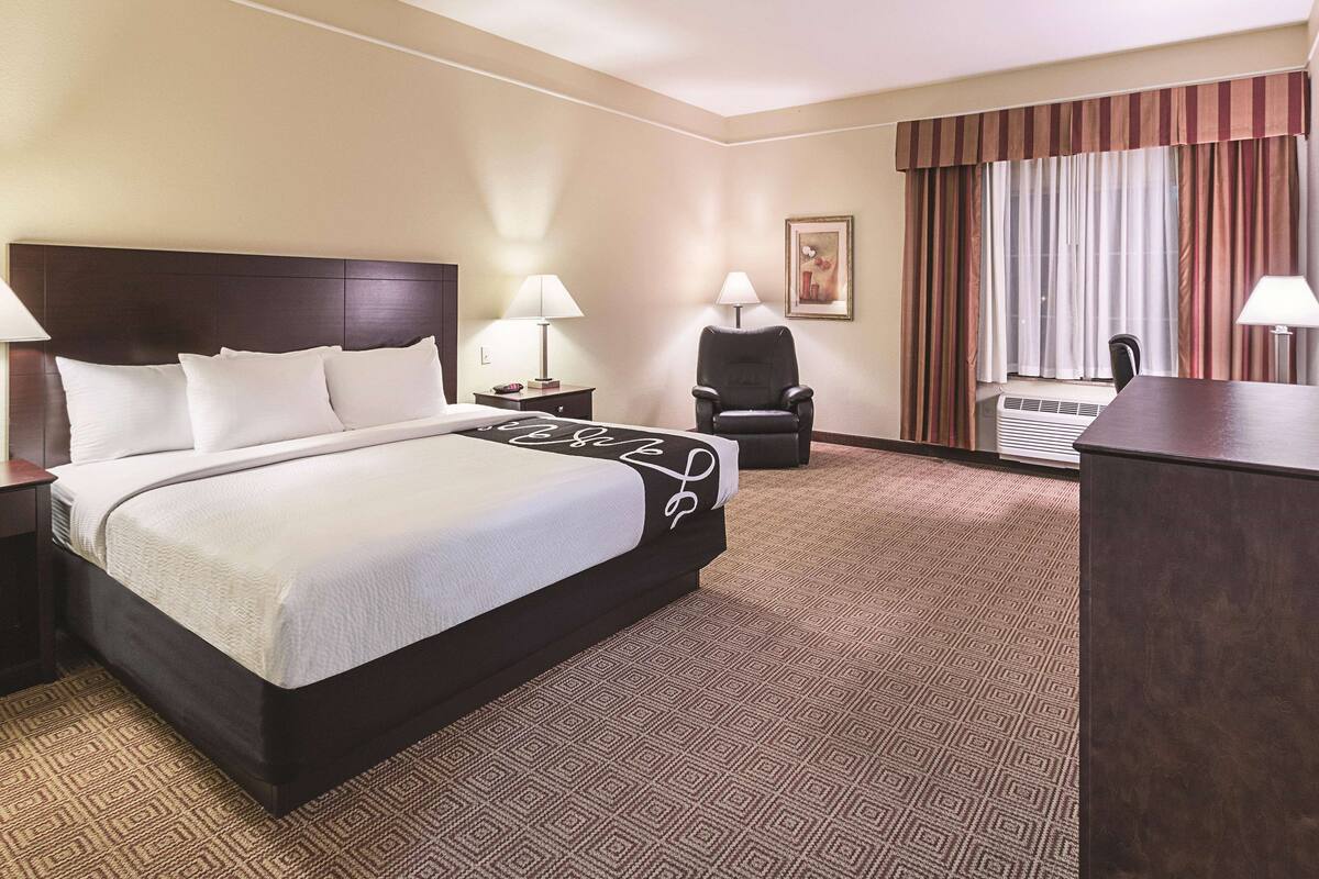 Una habitación de hotel con una cama grande, una silla, un escritorio y una ventana con cortinas.