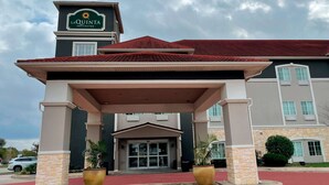 Entrada d'hotel amb zona d'espera coberta, un cartell de La Quinta Inn & Suites i un senyal de via contra incendis.