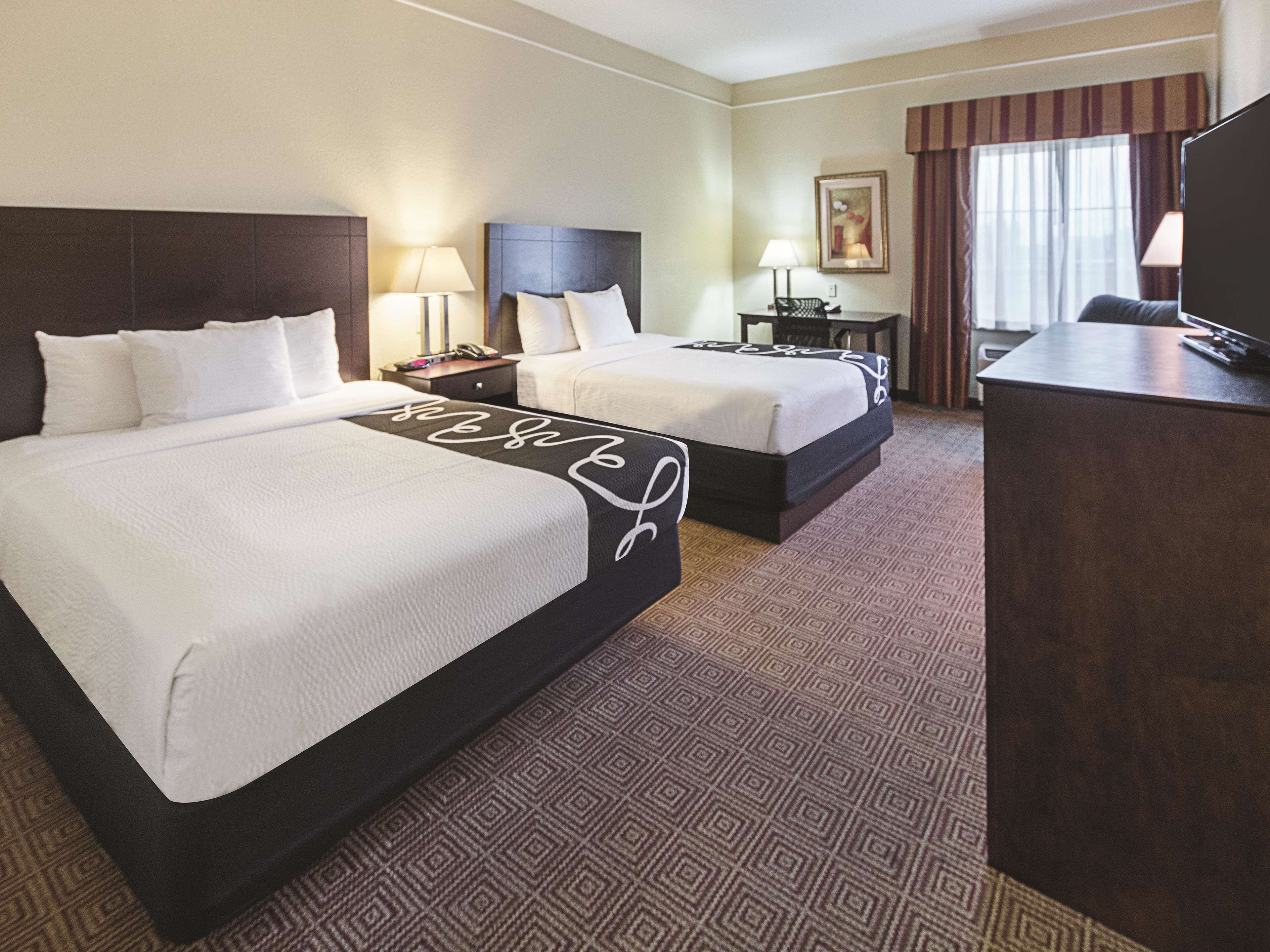 Quarto de hotel com duas camas, uma escrivaninha, uma cadeira e uma televisão.