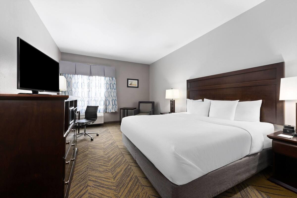 A hotel room with a large bed, a desk with a computer, a television, and a window with curtains.
