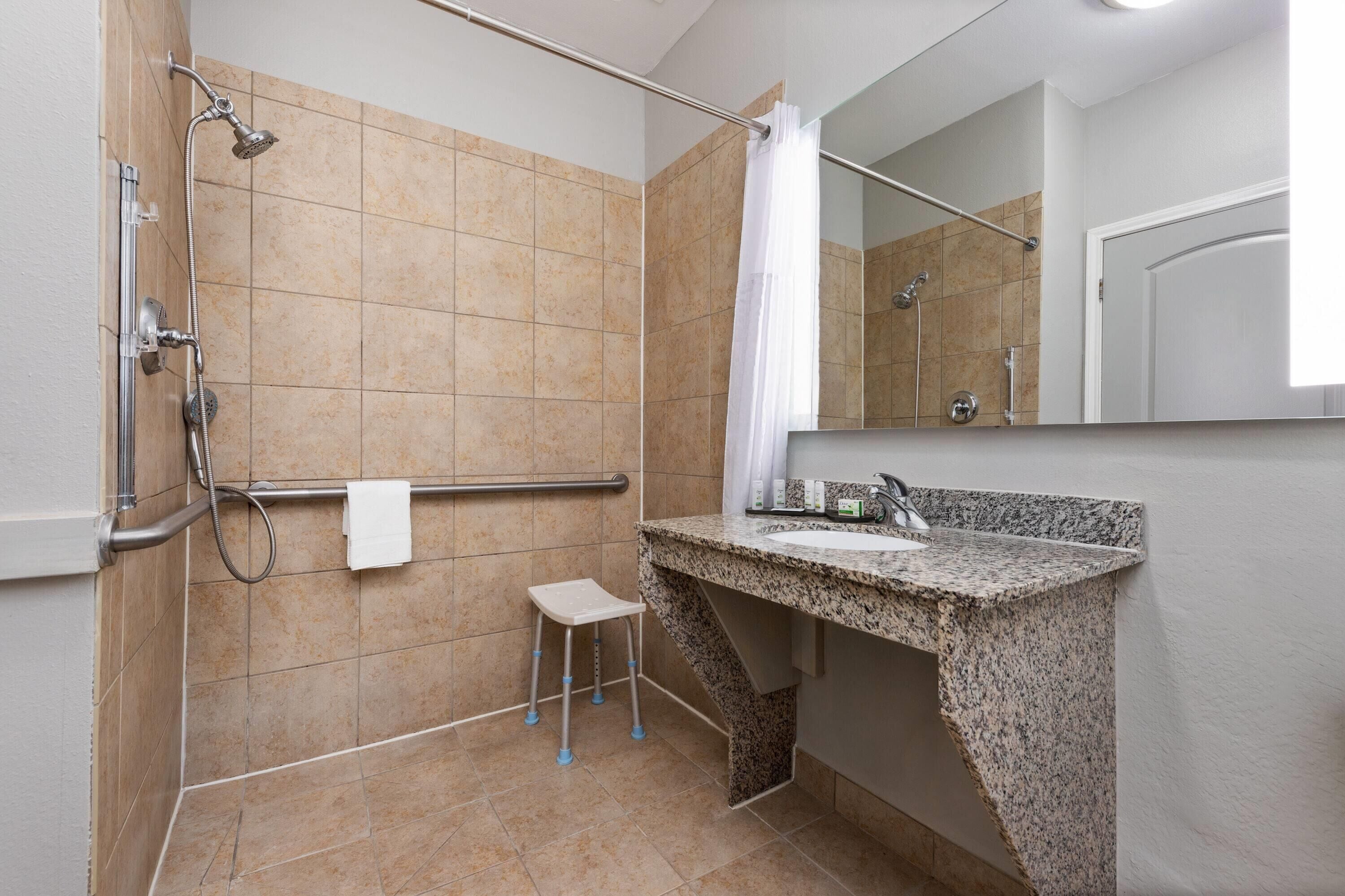 Un baño con ducha, lavamanos, espejo y toallero.