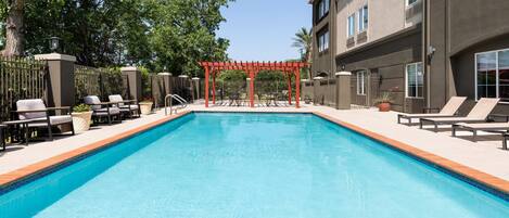 A rectangular swimming pool with a red pergola in the center, surrounded by lounge chairs and a fence.